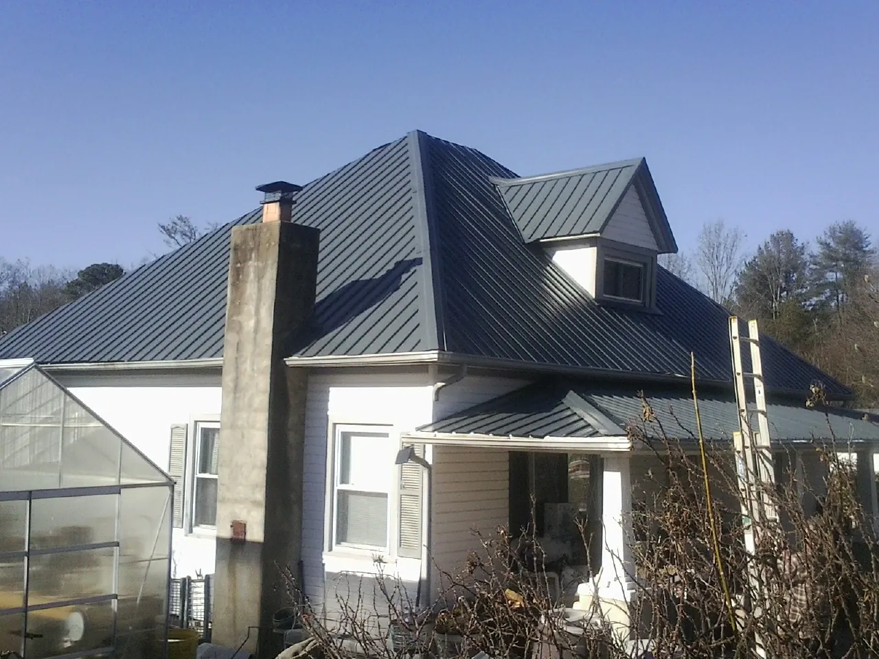 Dark blue standing seam metal roof on a white farmhouse with dormer — Slate & Tile Roof Repair by Roofing Brothers in Mandaree