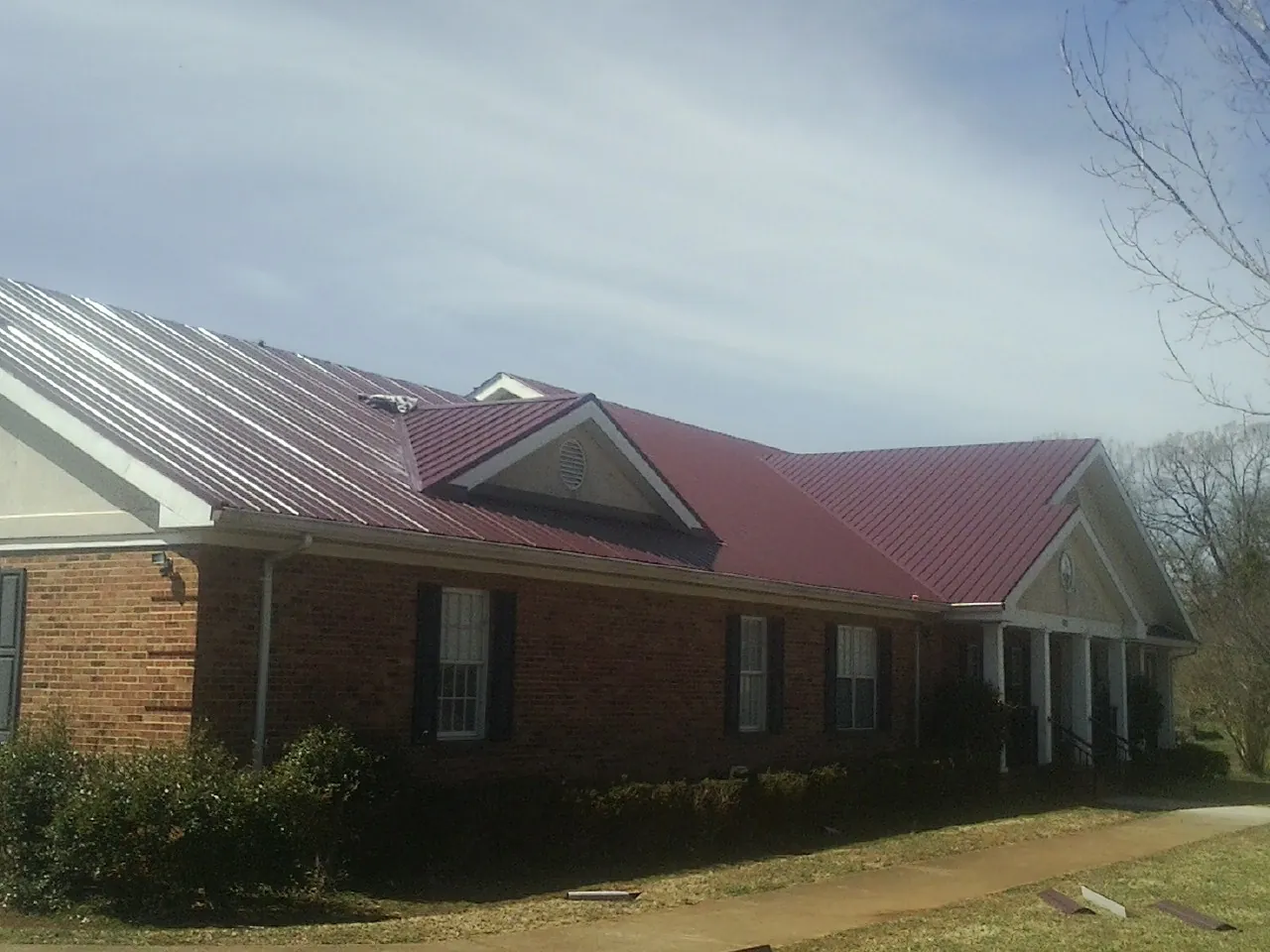 Red metal roof with gabled entries on a long brick building, from a Hail Damage Roof Repair job in Mandaree