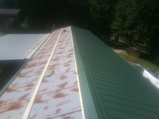 Old rusted panels beside newly installed green metal roofing — Wind Damage Roof Repair by Roofing Brothers in Mandaree