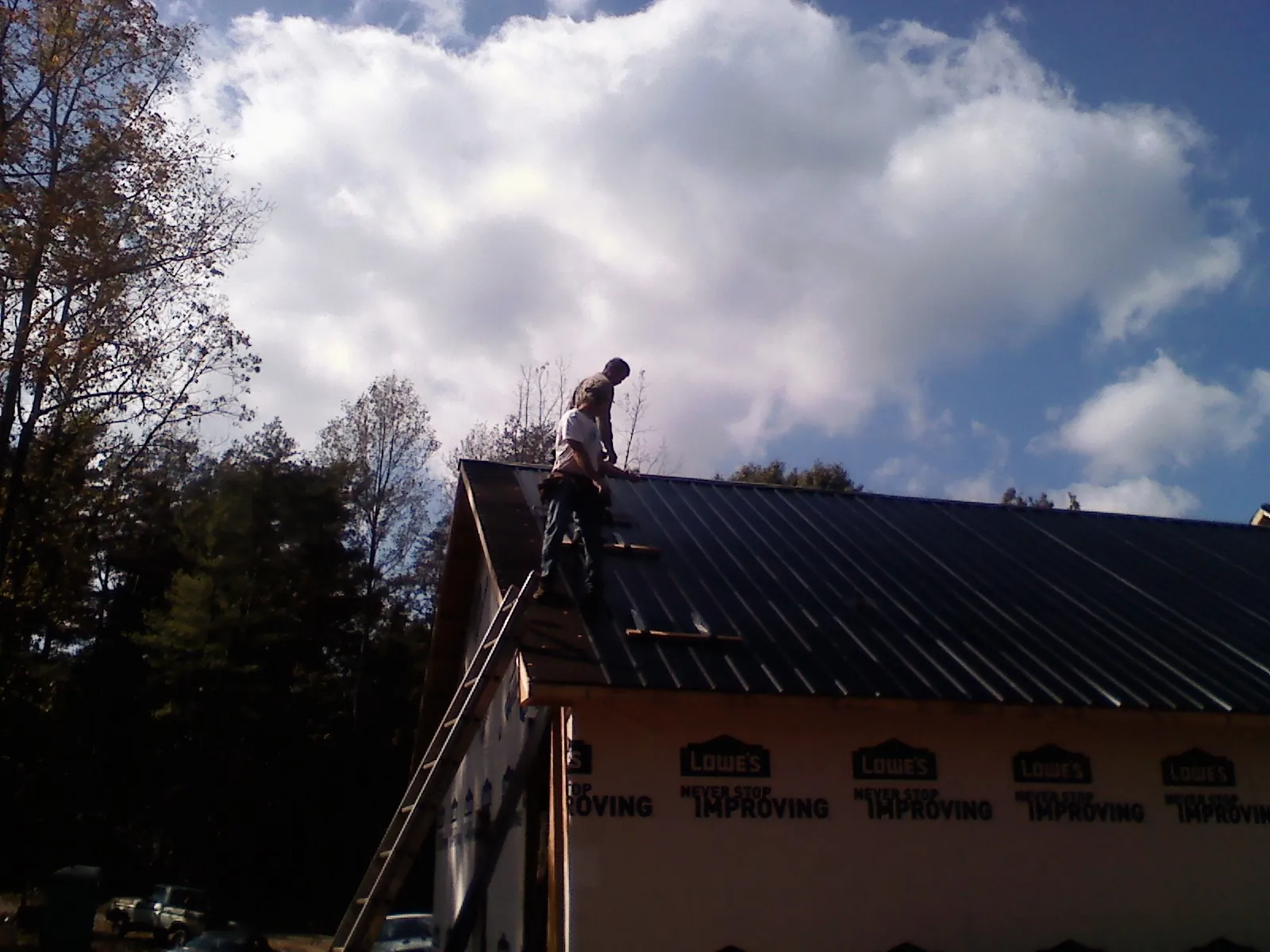 Roofer fastening dark metal panels high against a cloudy sky, from a Roof Inspection job in Mandaree