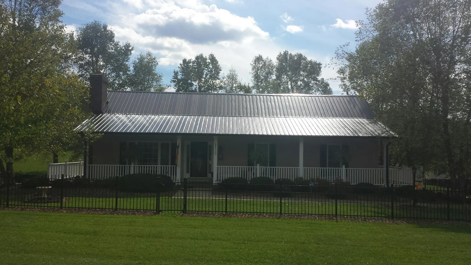 Gray metal roof on a brick ranch with a full width front porch — Gutter Guard Installation work by our crew in Mandaree
